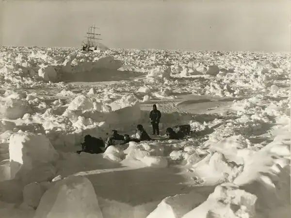 Explorer navigating icy Antarctic landscape with ship in background.