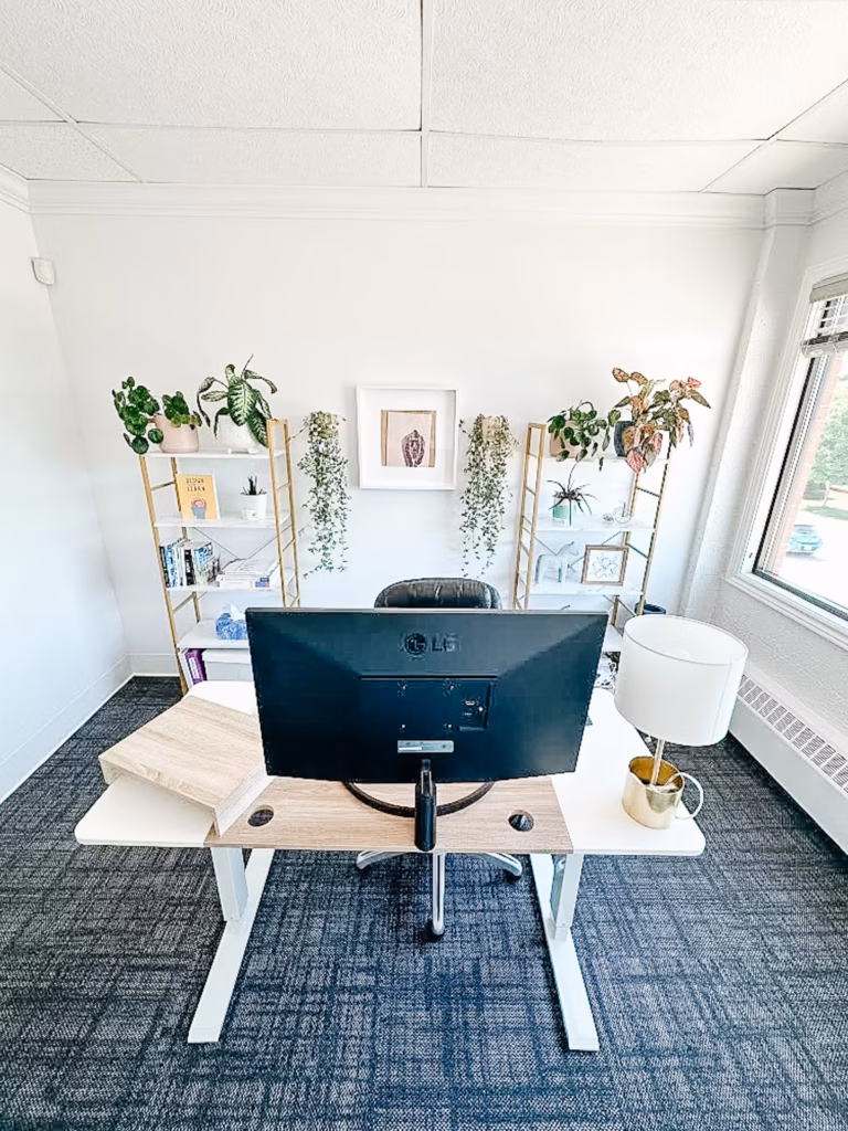 Modern home office with plants, white walls, gold shelving, and a standing desk.