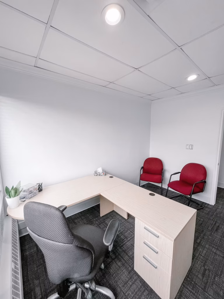 Modern office with L-shaped desk, ergonomic chair, red guest chairs, and drop ceiling.