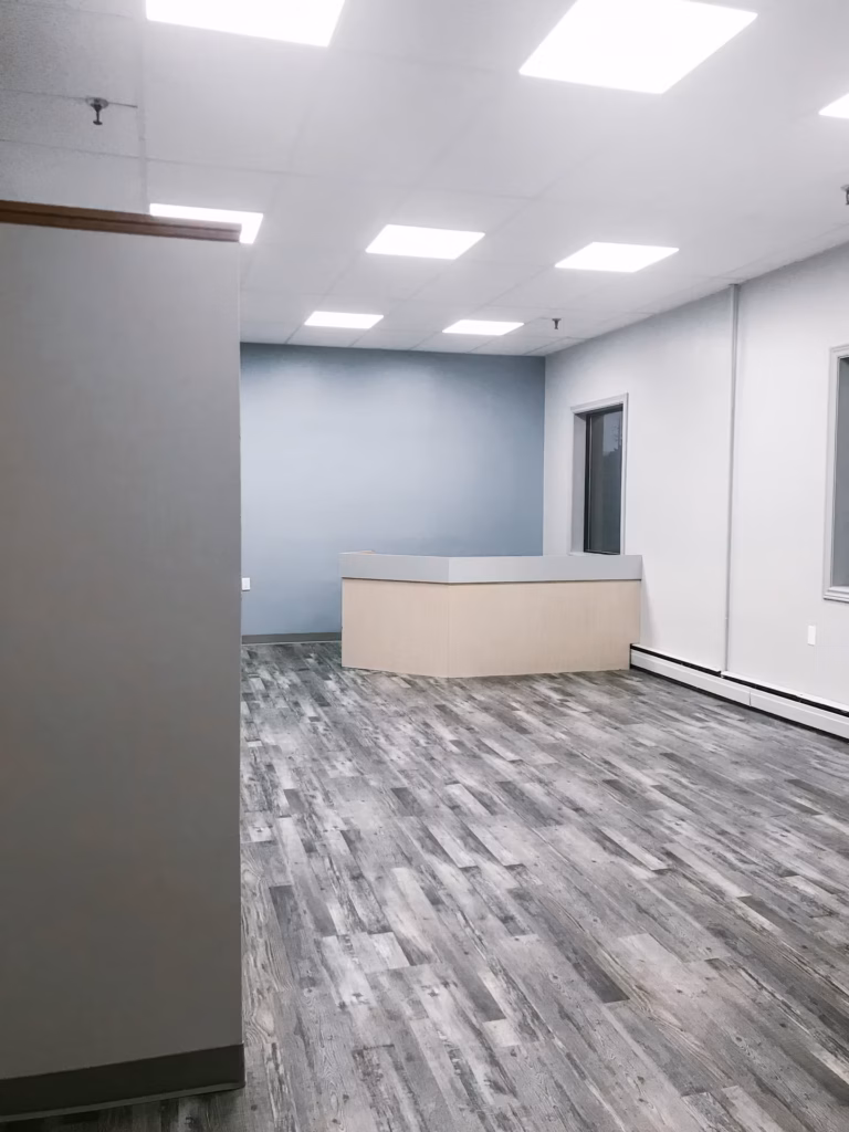 Empty office with grey wood floor, light blue wall, reception desk, and bright ceiling lights.