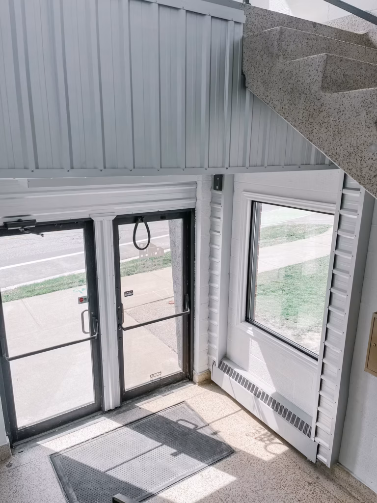 Building interior with corrugated metal walls, glass doors, window, and speckled stairs.