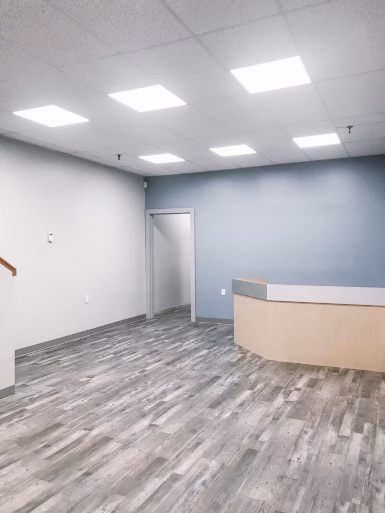 Empty office with wood floors, light blue wall, white walls, reception desk, and ceiling lights.