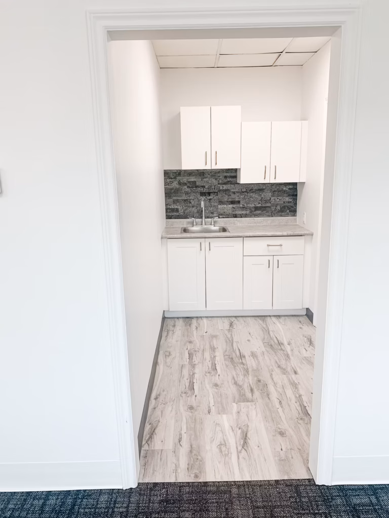 Small kitchen with white cabinets, gray backsplash, sink, and light wood-look floor.