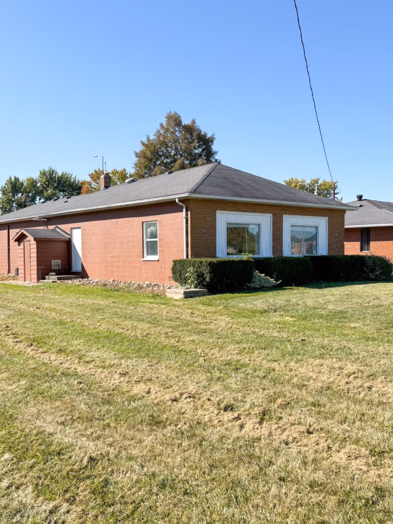 Brick house with dark roof, green lawn, and clear blue sky.