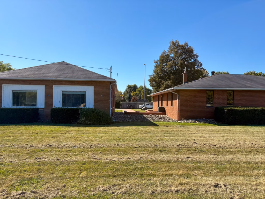 Two brick houses with green lawns under a clear blue sky.