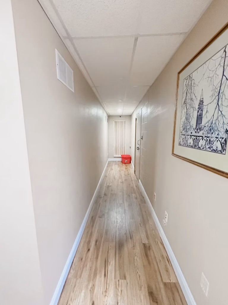 Long hallway with light wood floor, beige walls, white trim, and a framed winter scene painting.