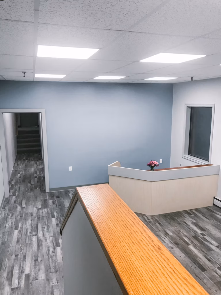 Modern office reception area with light blue walls, wood-look flooring, and a light wood reception desk.