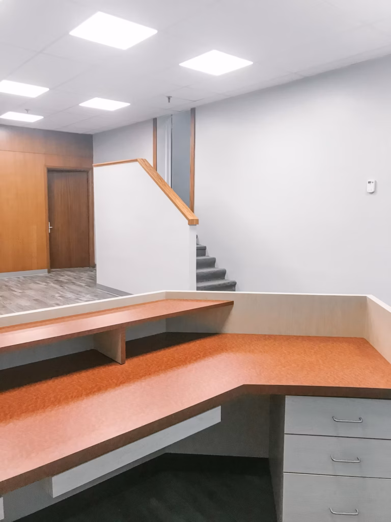 Modern office reception area with wood desk, light walls, carpeted stairs, and wood-paneled door.