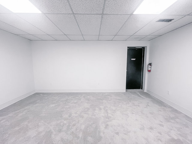 Spacious empty office room with white walls and gray carpet in South London.