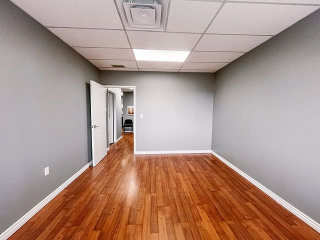 Empty office room with hardwood floors and gray walls.