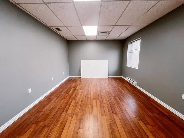 Empty office room with hardwood floors and gray walls.