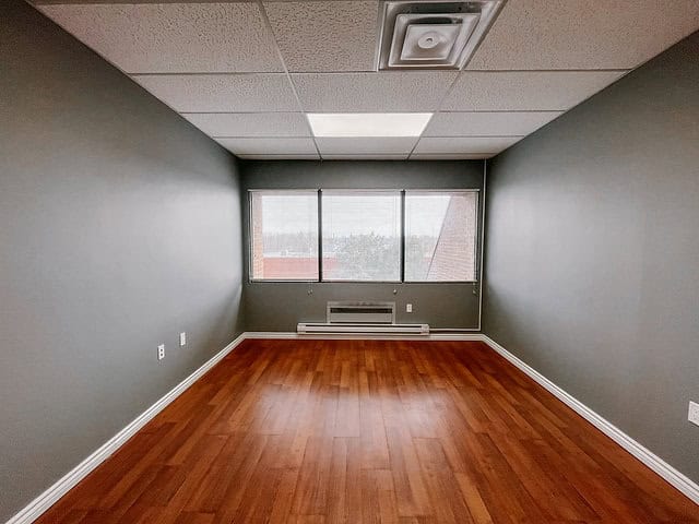 Empty office room with large window and hardwood floor.