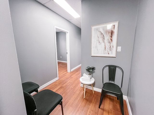 Modern office waiting area with two black chairs and a small table.