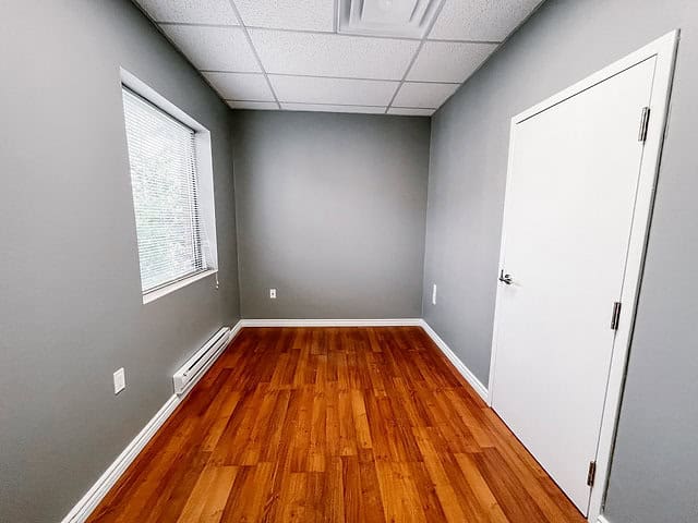 Empty office room with gray walls, wooden floor, and window.
