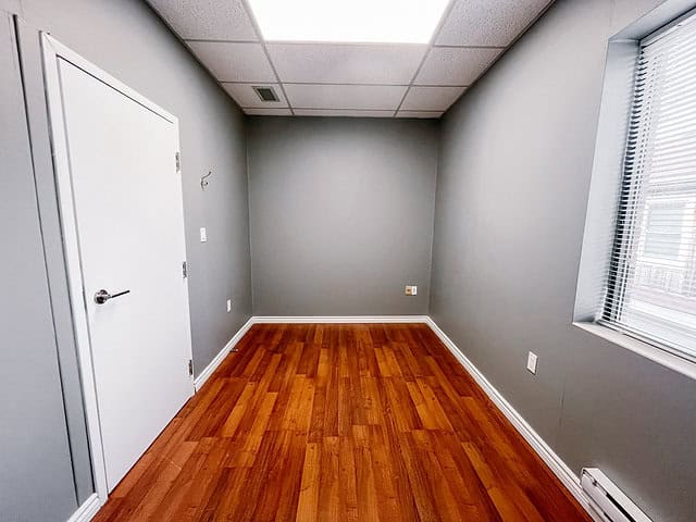 Empty office room with gray walls and wooden floor near window.