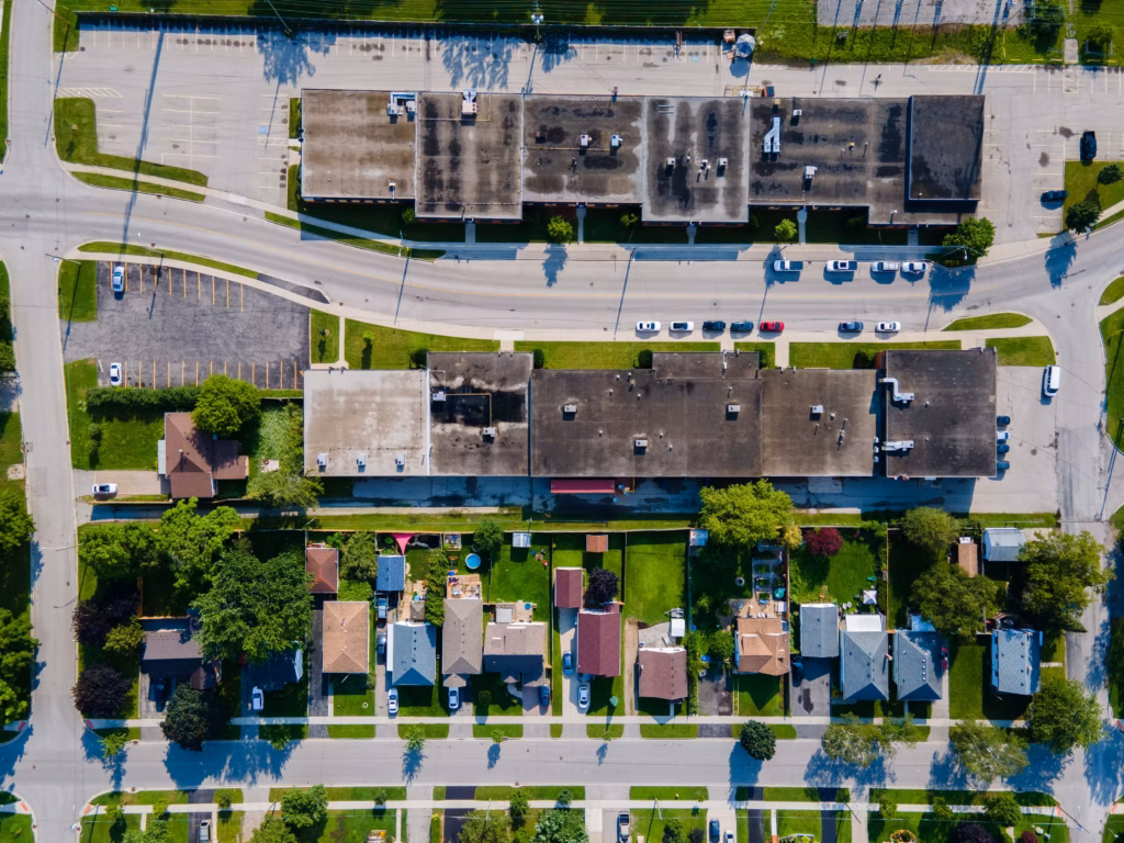 Aerial view of suburban neighborhood with houses, streets, parking lots, and commercial buildings.