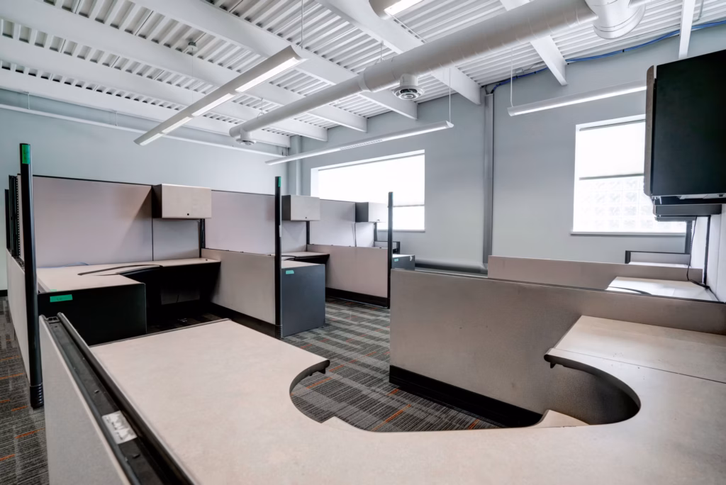 Modern office with cubicles, exposed ceiling, windows, and patterned carpet.