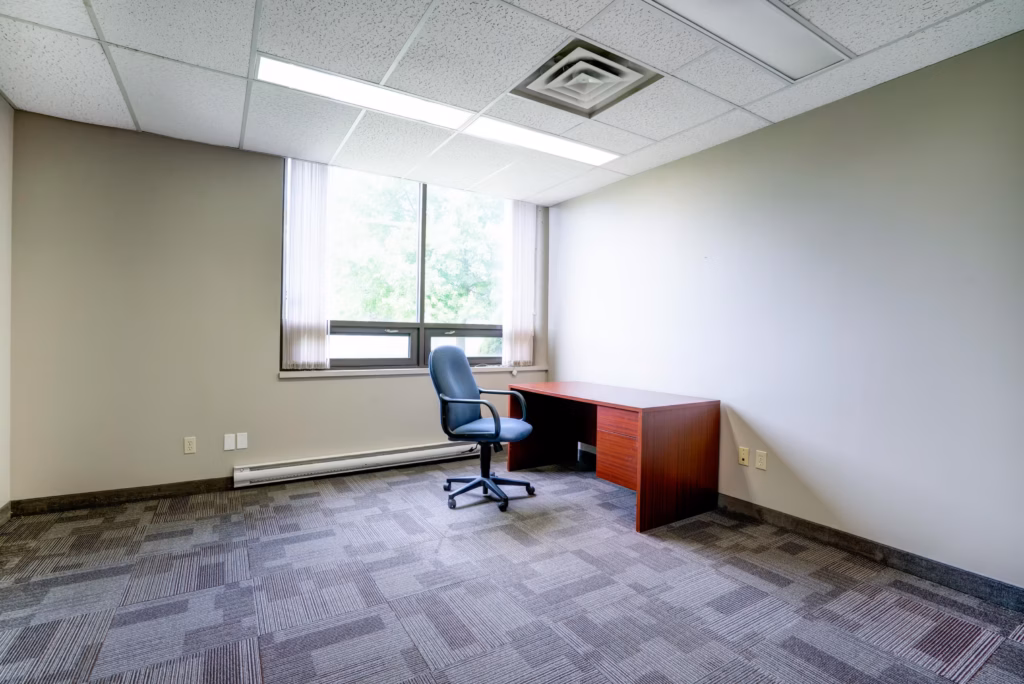 Empty office with window, desk, chair, and patterned carpet.