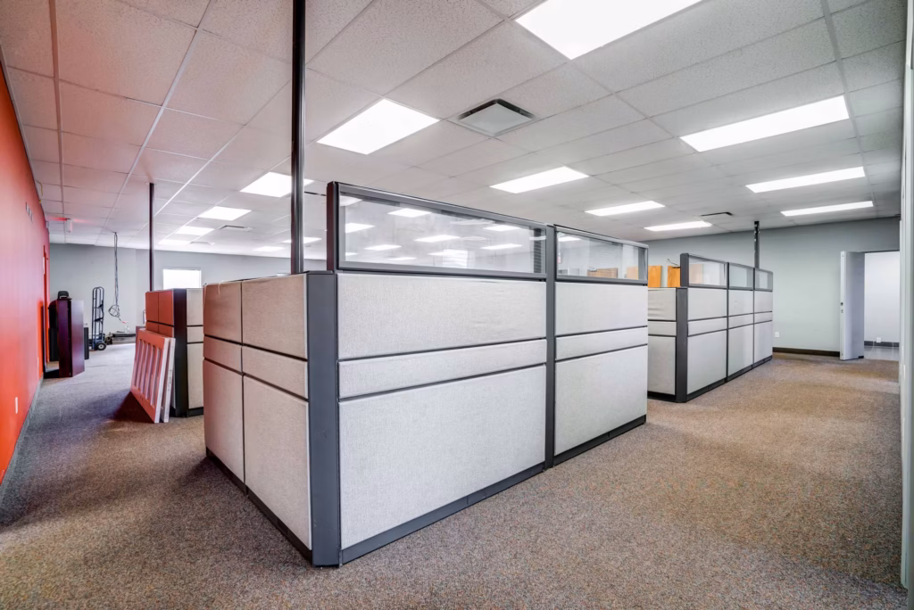 Empty office with cubicles, red accent wall, and gray carpet.