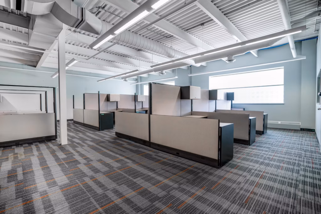 Modern office with cubicles, exposed ceiling ducts, and patterned carpet.